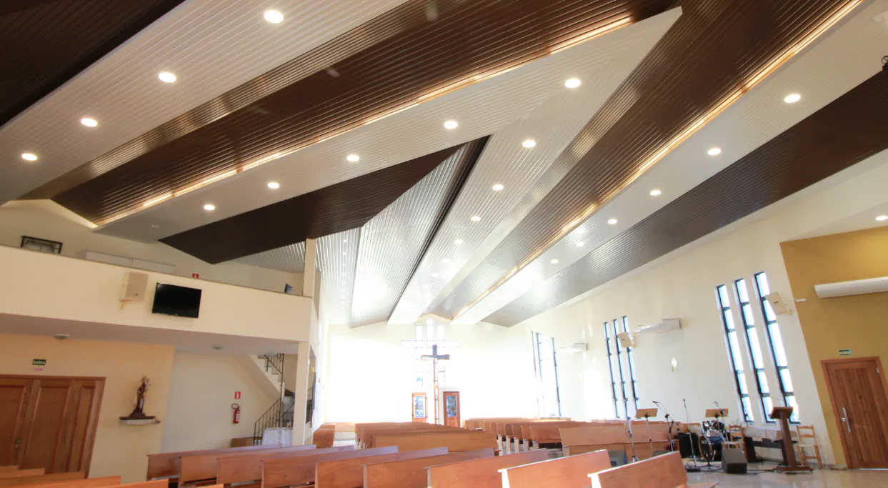 A Paróquia Nossa Senhora das Vitórias, em Curitiba/PR, investiu no Metalfort para transformar tanto a estética quanto a acústica do ambiente. Esse revestimento metálico de alumínio foi cuidadosamente projetado para aprimorar a inteligibilidade da fala, um aspecto crucial em espaços que valorizam a palavra falada, como as igrejas. Com uma ampla gama de opções de paginação e fabricação, o Metalfort oferece soluções técnicas eficientes para atender às demandas acústicas específicas da Paróquia Nossa Senhora das Vitórias. Além de sua função acústica, o Metalfort apresenta um design moderno que se harmoniza com a estética da madeira. Com sua durabilidade, resistência ao fogo, imunidade a pragas e propriedades térmicas, o Metalfort cria um ambiente harmonioso e otimizado acusticamente para a Paróquia Nossa Senhora das Vitórias.